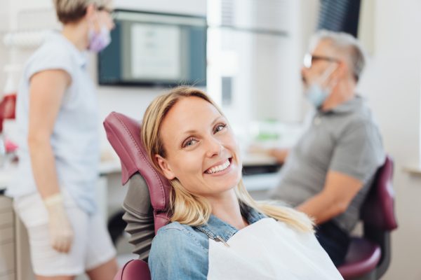 patient smiling in dental chair while dentists speak behind her